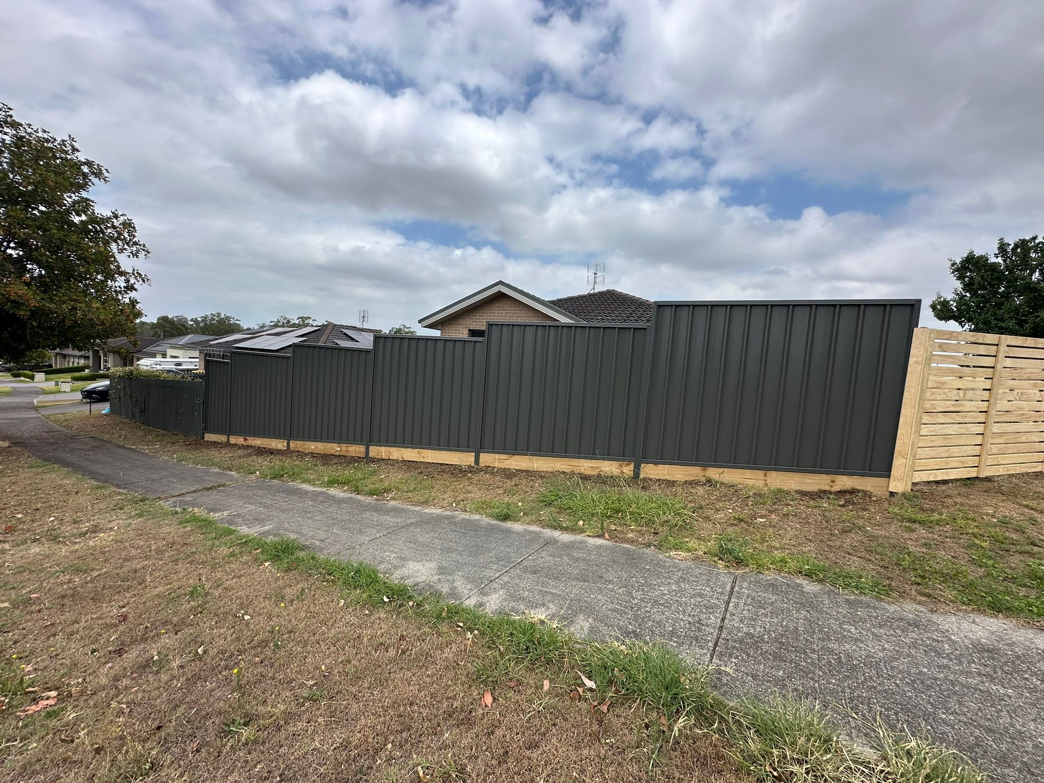 Stepped Colorbond fence on timber sleepers along a street frontage with a timber slat return panel