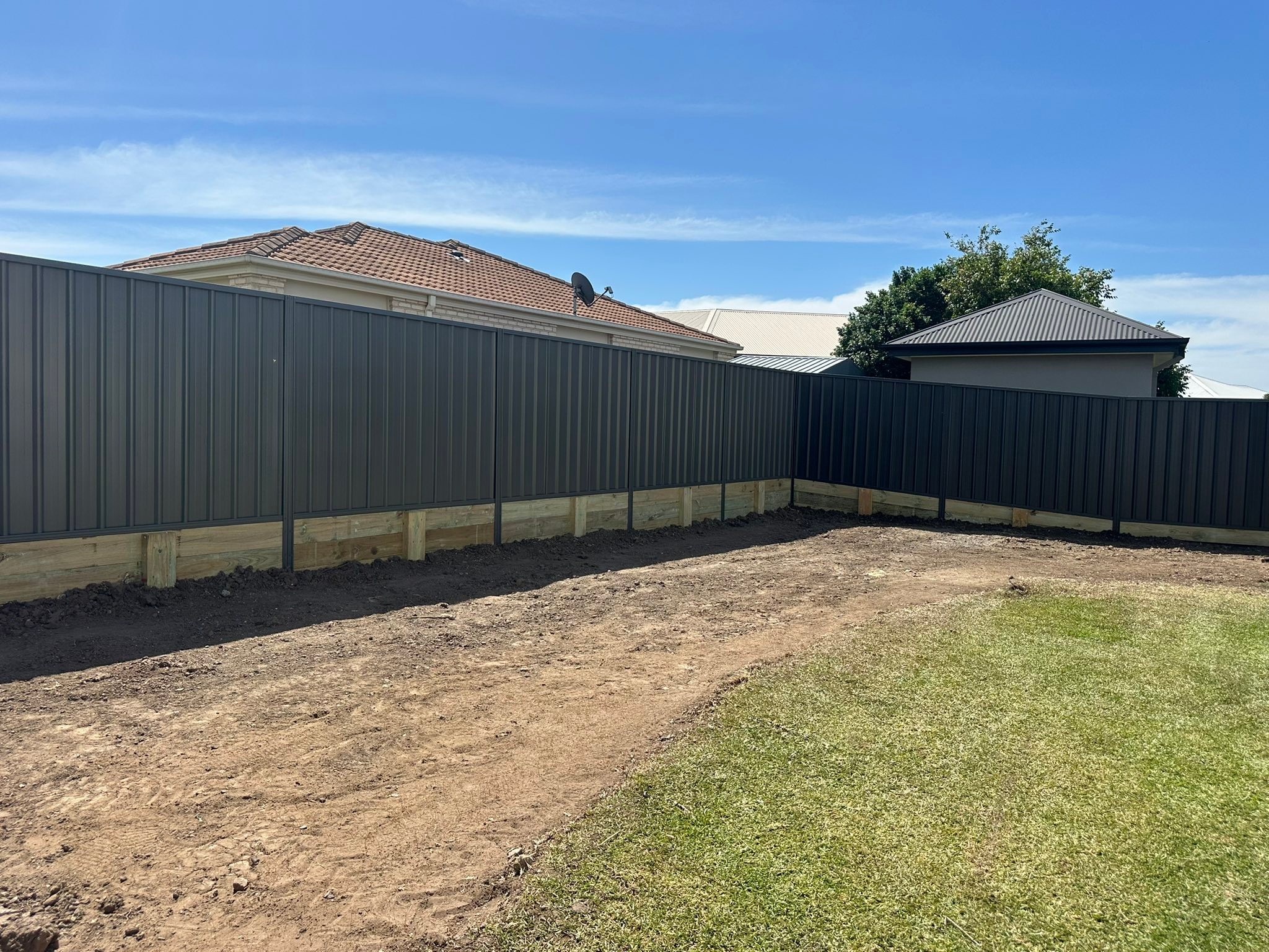 Dark Colorbond fence sitting on a new timber sleeper retaining wall in a back yard