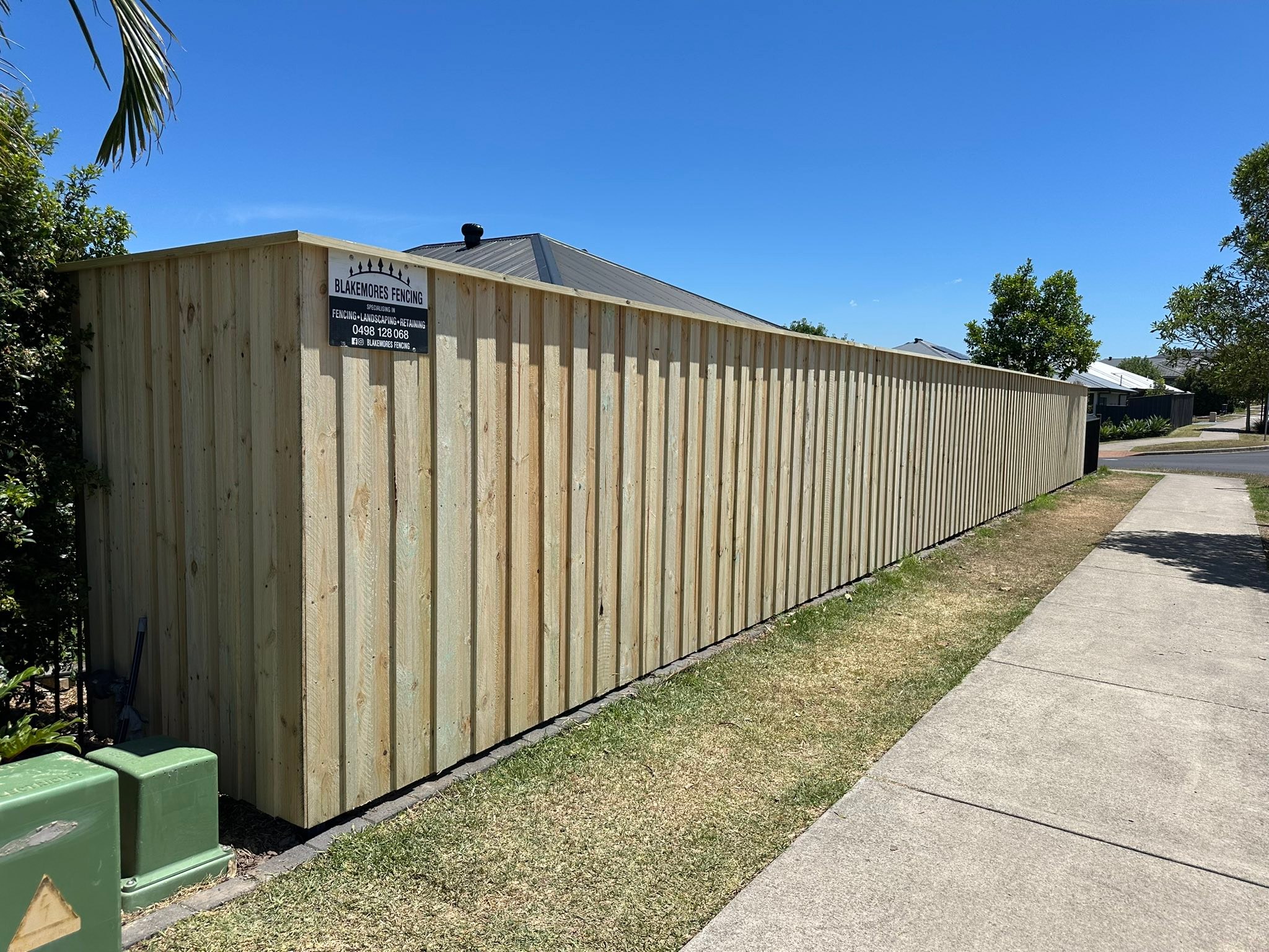 Long lap and cap treated pine paling fence with the Blakemores Fencing sign fixed to it