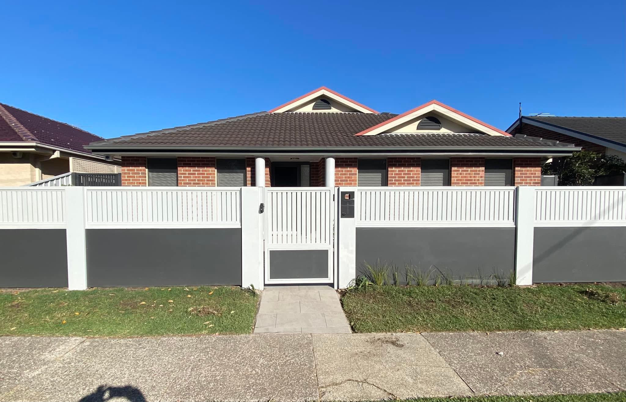 Modular wall in white and grey rendered panels with a white aluminium slat gate across a house frontage