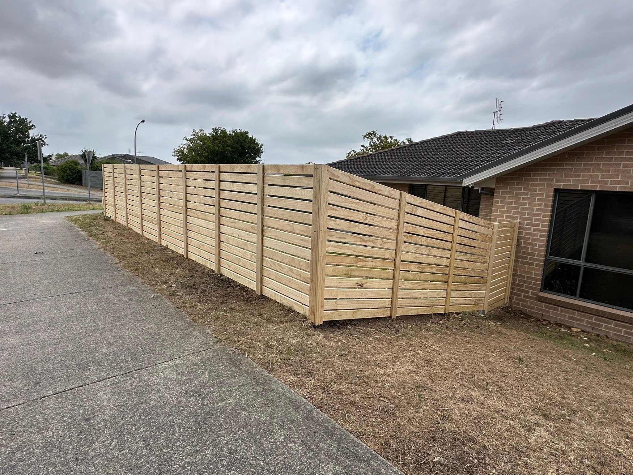 Treated pine horizontal slat fence raked down a slope beside a brick home